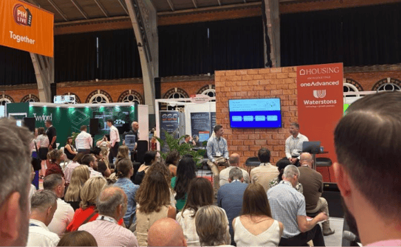 A photo of Platform Housing and Voicescape speaking at a conference talk inside the Housing Annual 2026 Conference Hall.